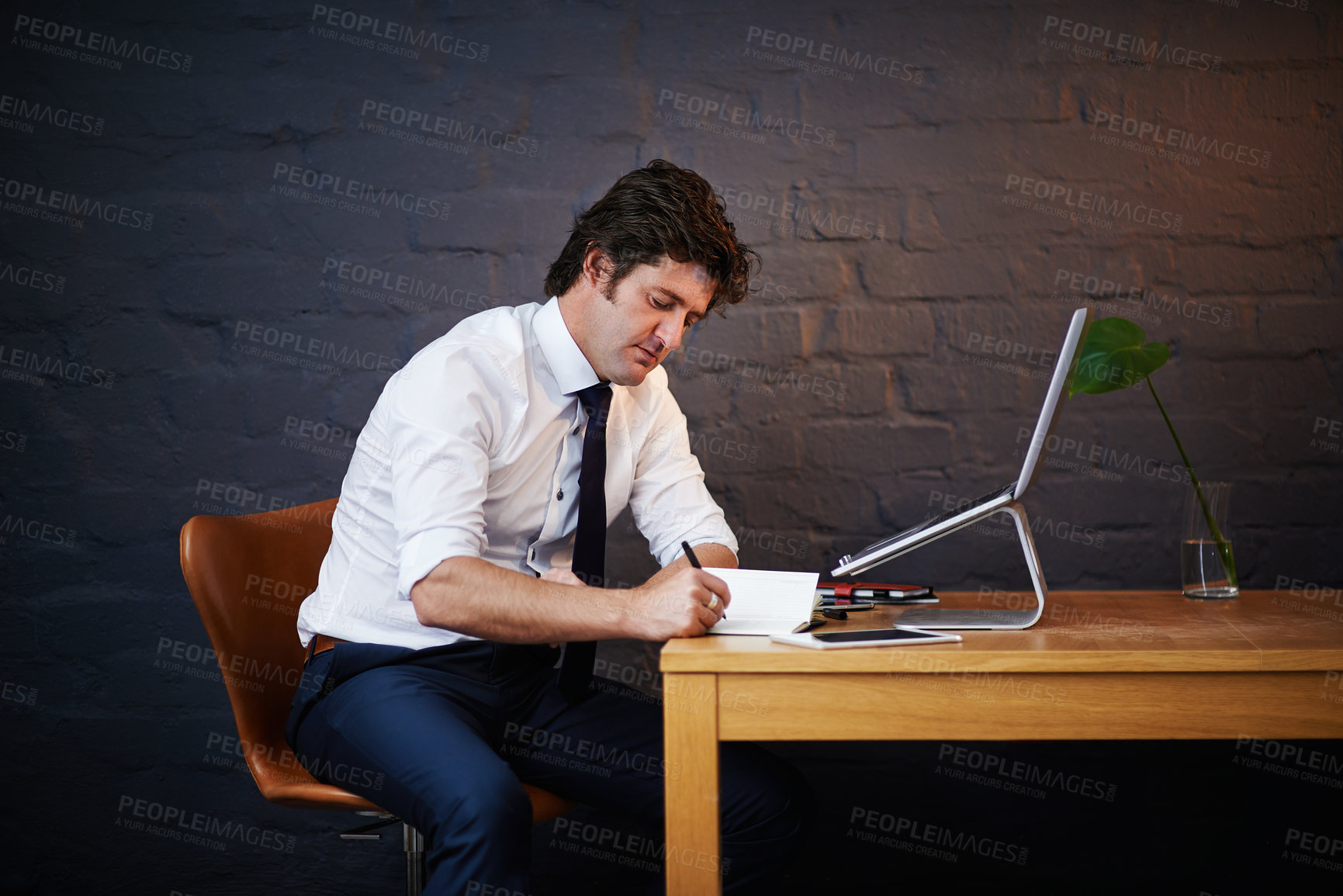 Buy stock photo Desk, investigation and notebook with detective man in office at night to work on criminal report. Brick wall, laptop and writing with mature investigator at table for evidence, justice or research