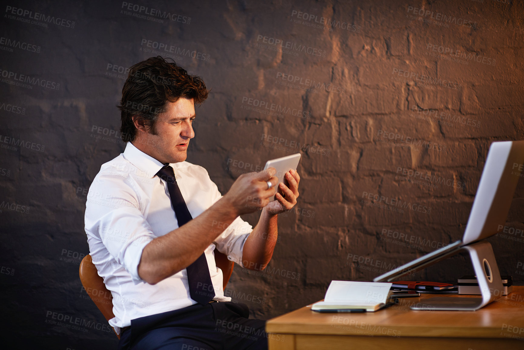 Buy stock photo Desk, investigation and tablet with detective man in office at night to work on criminal report. Brick wall, information and laptop with mature investigator at table for evidence, justice or research