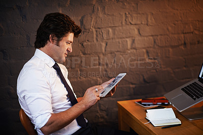Buy stock photo Shot of a businessman working on his digital tablet late at night