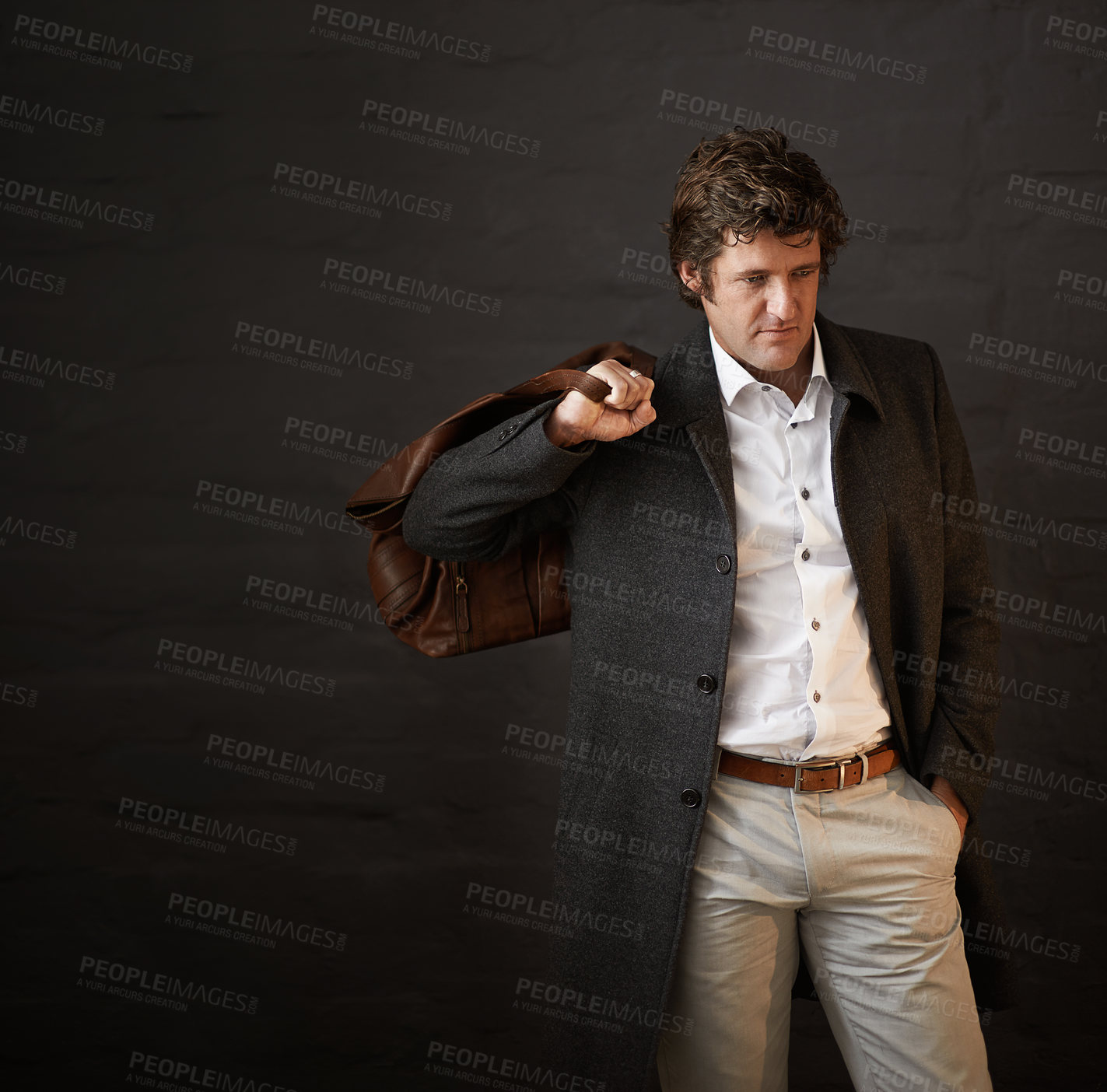 Buy stock photo Shot of a well dressed businessman carrying a bag against a dark background