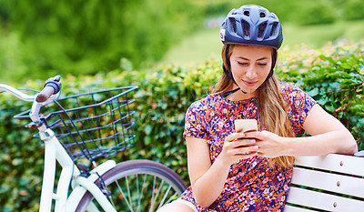 Buy stock photo Shot of a young woman using a phone while out for a cycle in the park