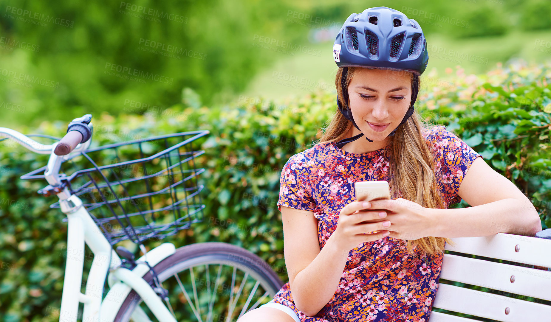 Buy stock photo Smartphone, bicycle and woman on bench in park with helmet, smile and online chat with connectivity. Communication, relax and happy girl checking social media with bike, phone or mobile app in nature