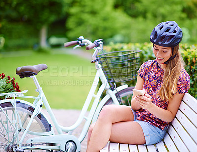 Buy stock photo Phone, bike and woman on bench in park with helmet, smile and online chat with connectivity. Communication, relax and happy girl checking social media with bicycle, smartphone or mobile app in nature