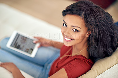 Buy stock photo High angle portrait of a young woman using her tablet while relaxing at home