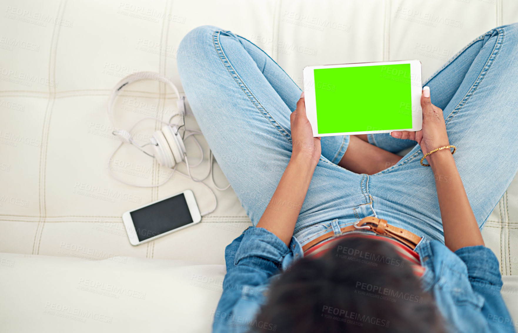 Buy stock photo High angle shot of a young woman using her digital tablet while sitting on the sofa