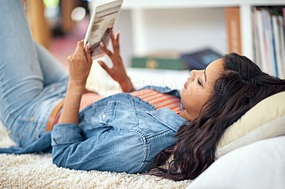 Buy stock photo Shot of a young woman using her digital tablet while lying on the sofa