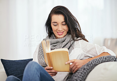 Buy stock photo Shot of a young woman reading a book while sitting in the living room