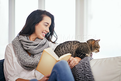 Buy stock photo Shot of a young woman reading a book with her cat next to her