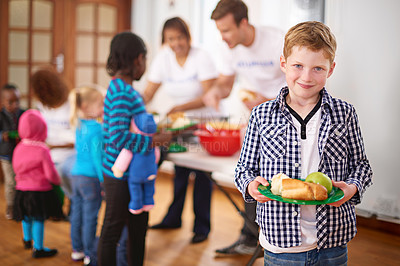 Buy stock photo Portrait of a little boy with a plate of food with volunteers serving food in the background