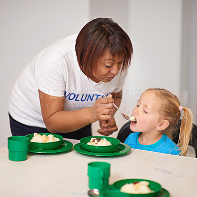 Buy stock photo Shot of a volunteer feeding a little girl at a youth center
