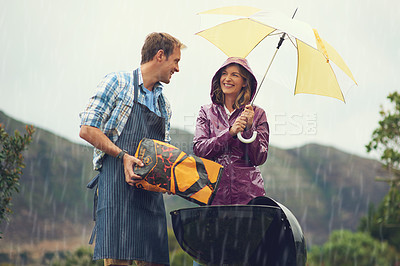 Buy stock photo Man, woman and barbecue in rain with umbrella, charcoal or surprise on vacation with love in garden. Couple, outdoor and grill in storm, backyard or cooking in winter with helping hand, wind or smile
