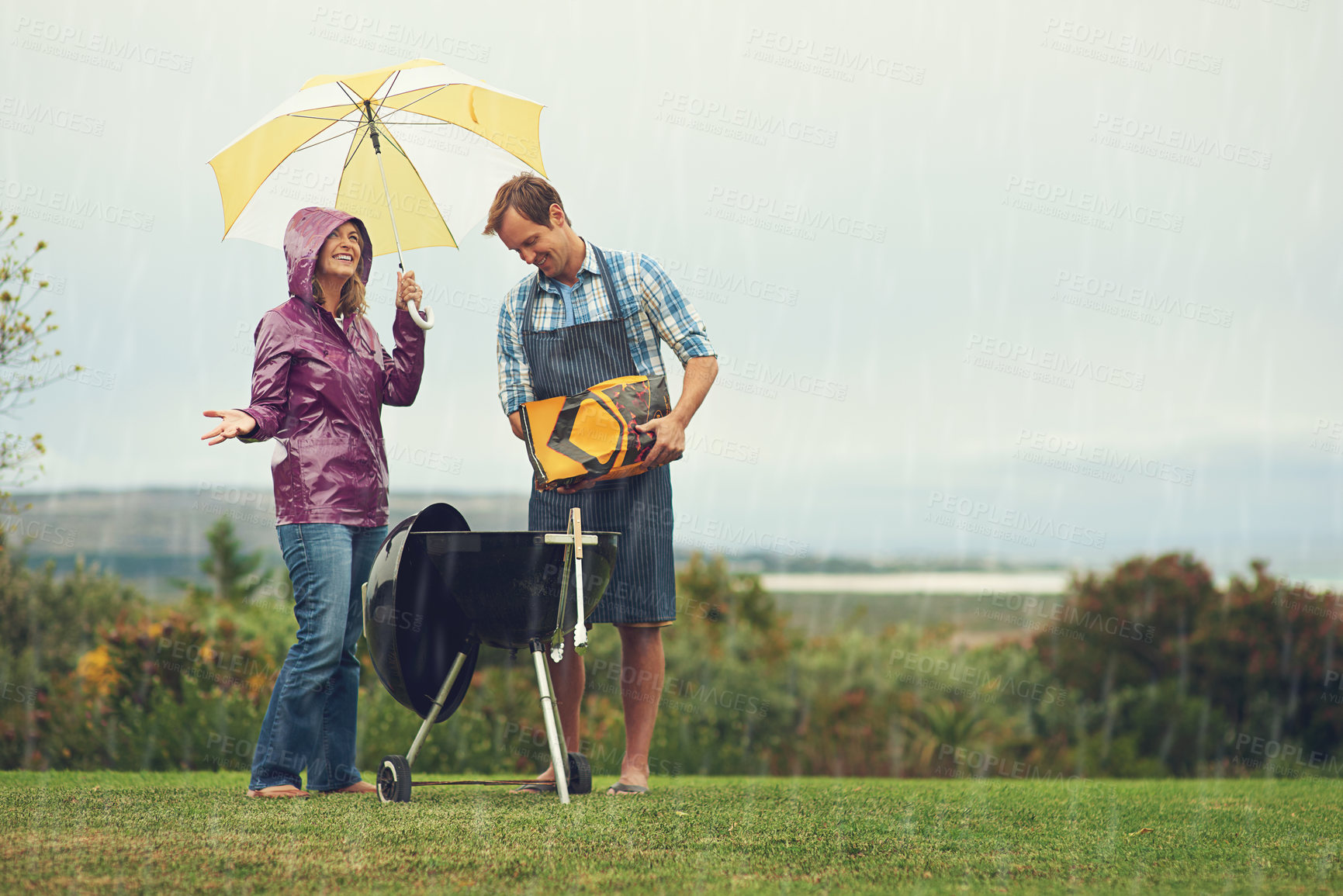 Buy stock photo Shot of a couple happily  barbecuing in the rain