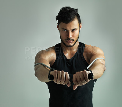 Buy stock photo Studio shot of a young man working out with a resistance band against a gray background