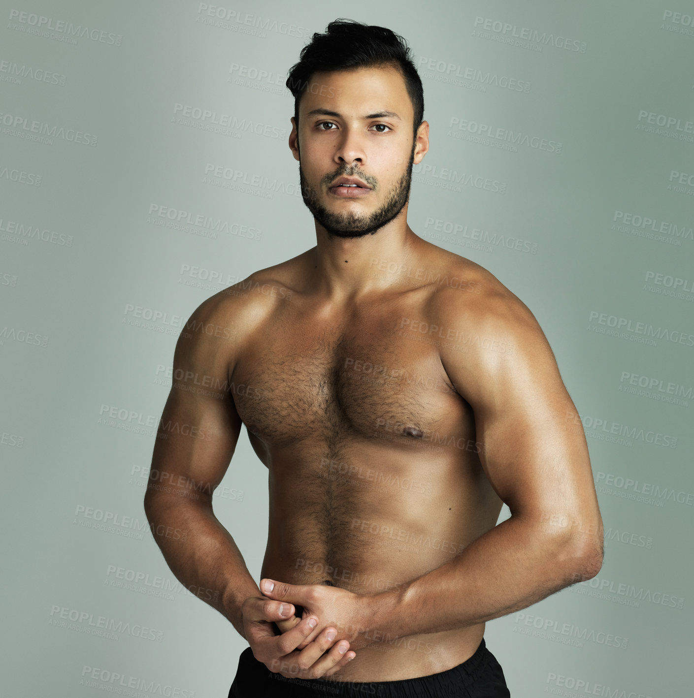 Buy stock photo Studio shot of an athletic young man flexing his muscles against a gray background