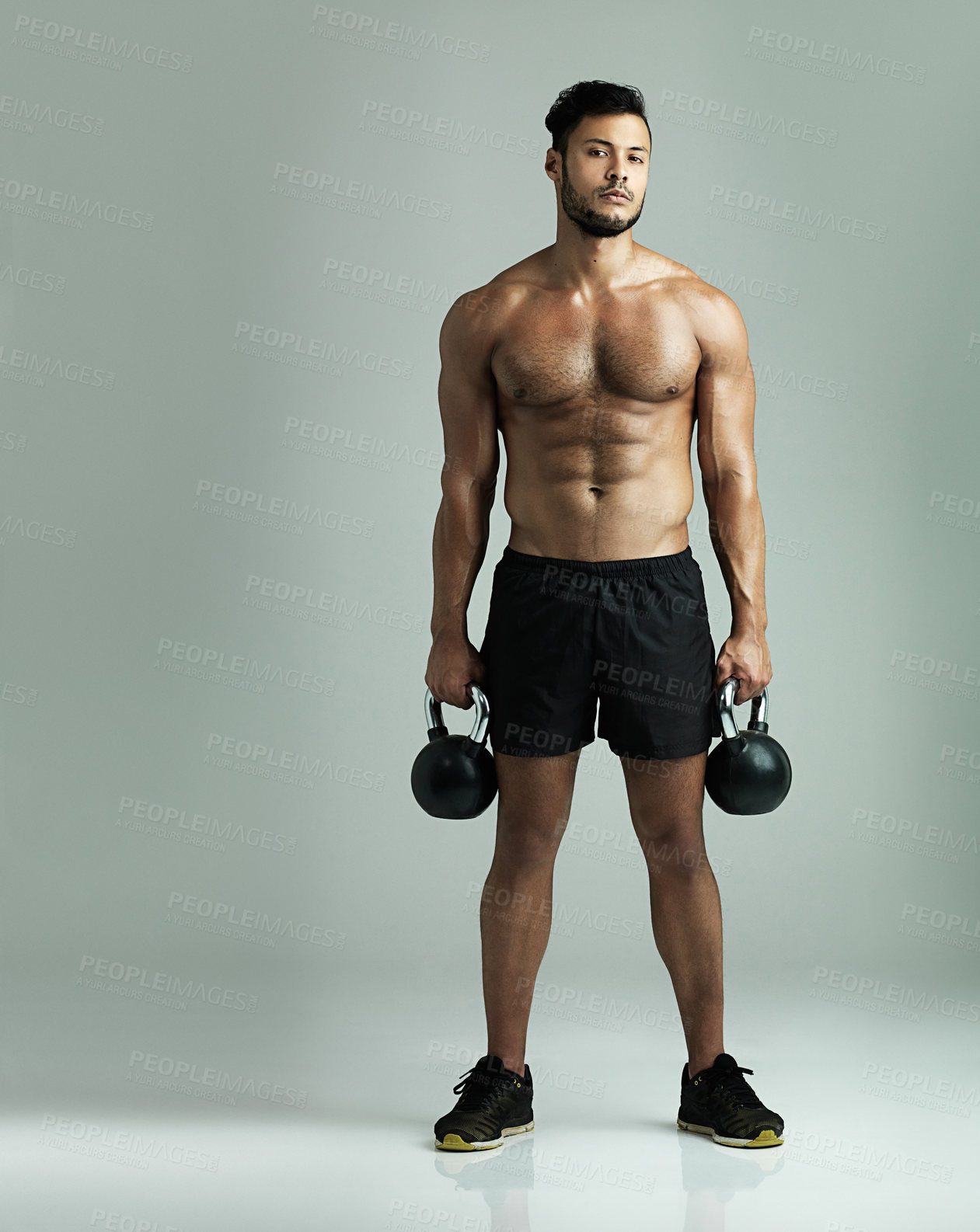Buy stock photo Studio shot of a young man working out with kettle bells against a gray background