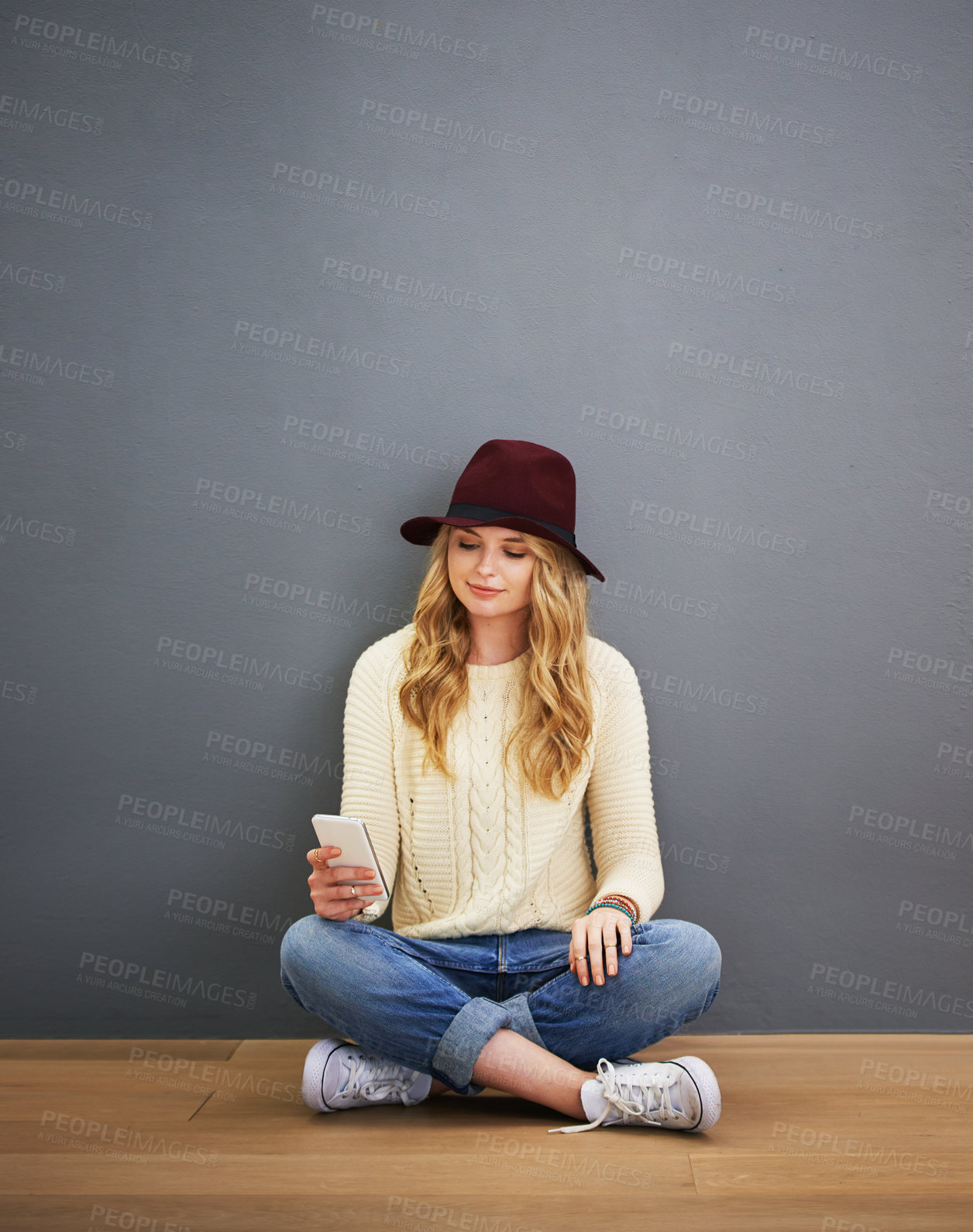 Buy stock photo Shot of a young woman using her cellphone while sitting against a gray background