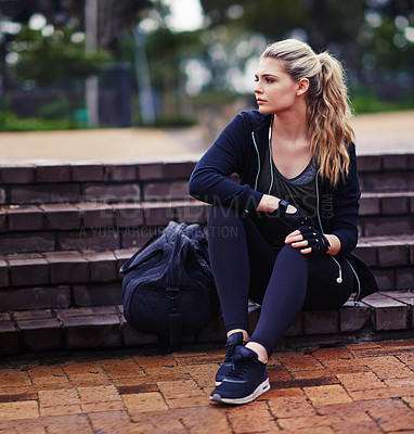 Buy stock photo Shot of a sporty young woman sitting outside with a gym bag