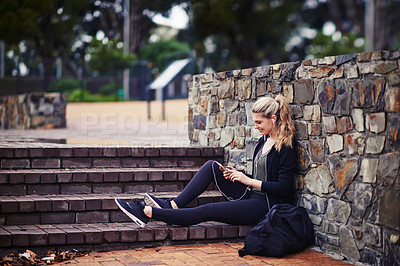 Buy stock photo Shot of a sporty young woman listening to music while sitting outside