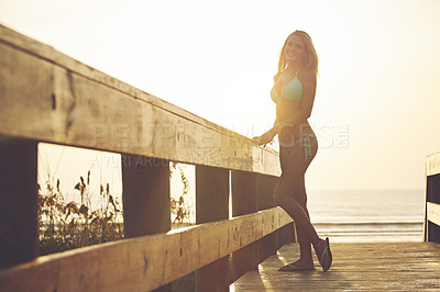 Buy stock photo Shot of a young woman in a bikini on a walkway near the beach