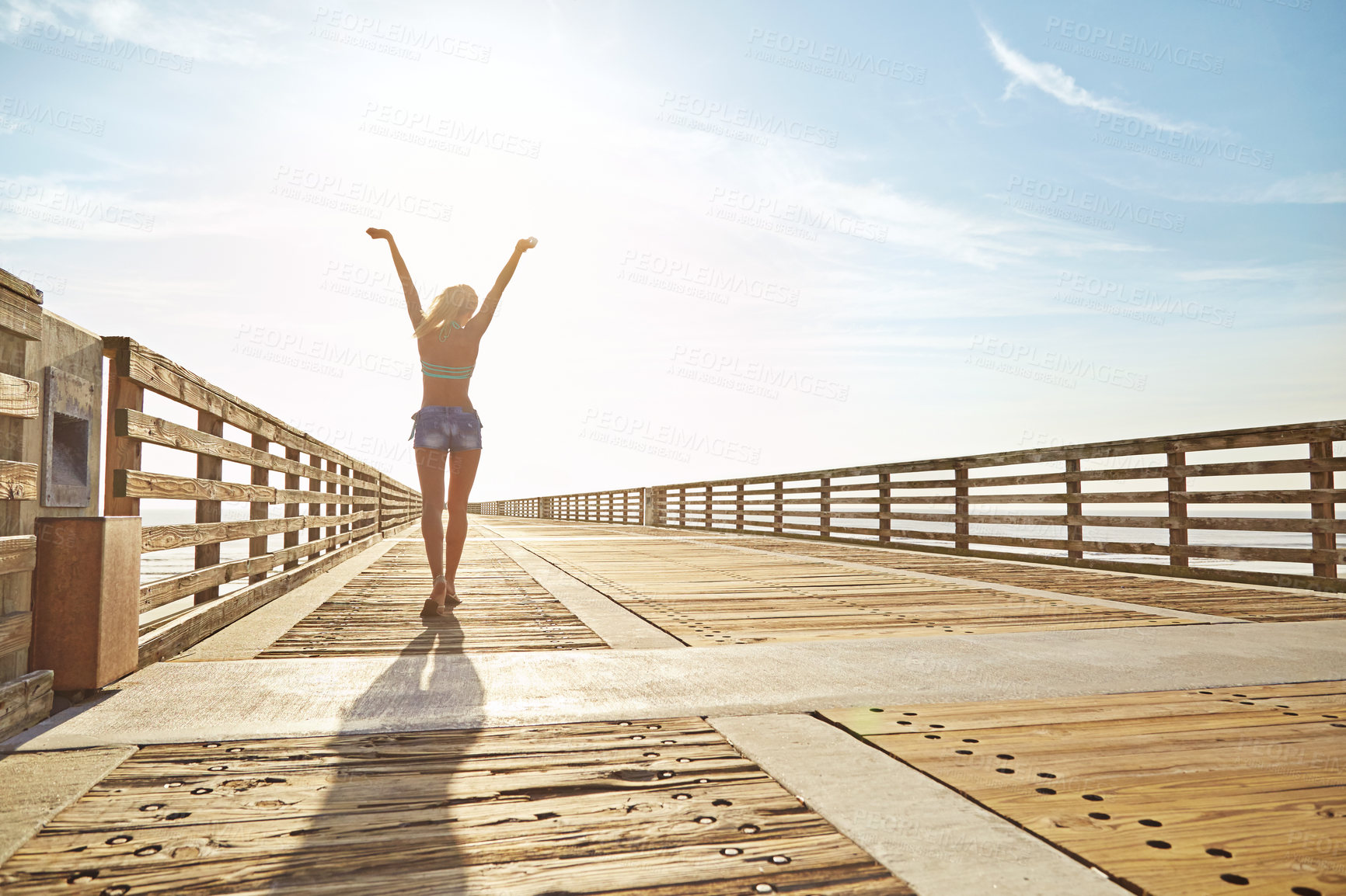 Buy stock photo Shot of a young woman in a bikini on a walkway near the beach