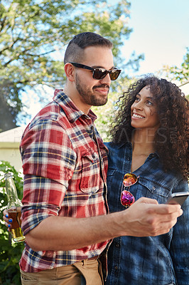 Buy stock photo Shot of a young man sharing something on his cellphone with his girlfriend