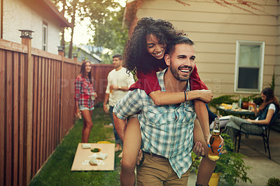 Buy stock photo Shot of a young man piggybacking his girlfriend with people standing in the background