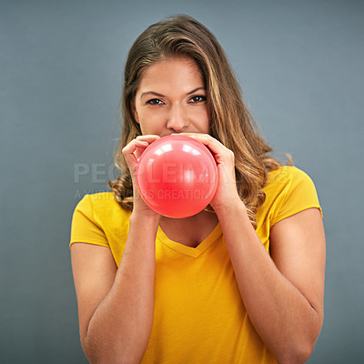 Buy stock photo Shot of a young woman inflating a balloon against a gray background