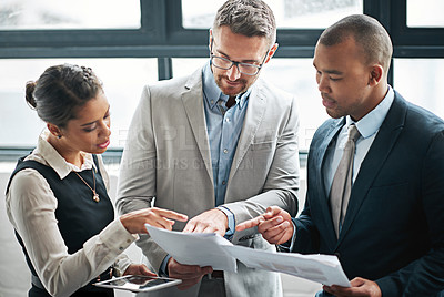 Buy stock photo Cropped shot of three businesspeople looking over some paperwork in the office