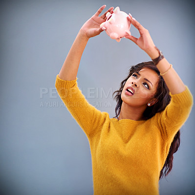 Buy stock photo Studio shot of a young woman looking up at her piggybank against a gray background