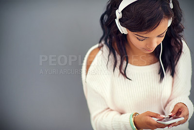 Buy stock photo Studio shot of a young woman listening to music while using her phone against a gray background