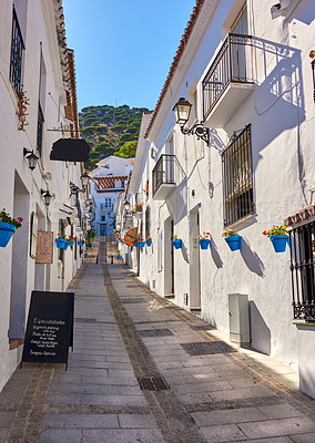 Buy stock photo Buildings, street and alley outside with architecture, travel and exploration with blue sky and aesthetic. Infrastructure, village and road outdoor for holiday, walkway and tourist location in Spain