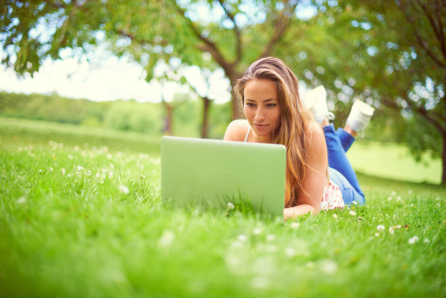 Buy stock photo Shot of a young woman using her laptop at the park