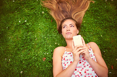 Buy stock photo Shot of a young woman using her cellphone while lying on the grass