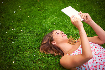 Buy stock photo Shot of a young woman using her digital tablet while lying on the grass