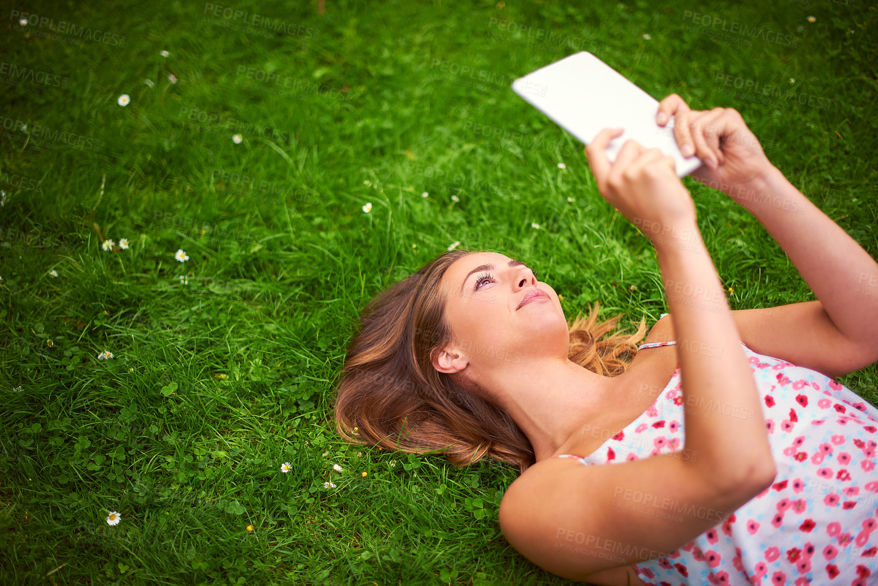 Buy stock photo Shot of a young woman using her digital tablet while lying on the grass
