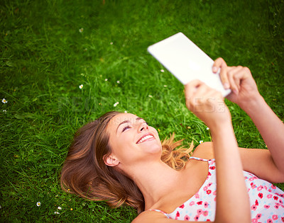 Buy stock photo Cropped shot of a young woman using her digital tablet while lying on the grass