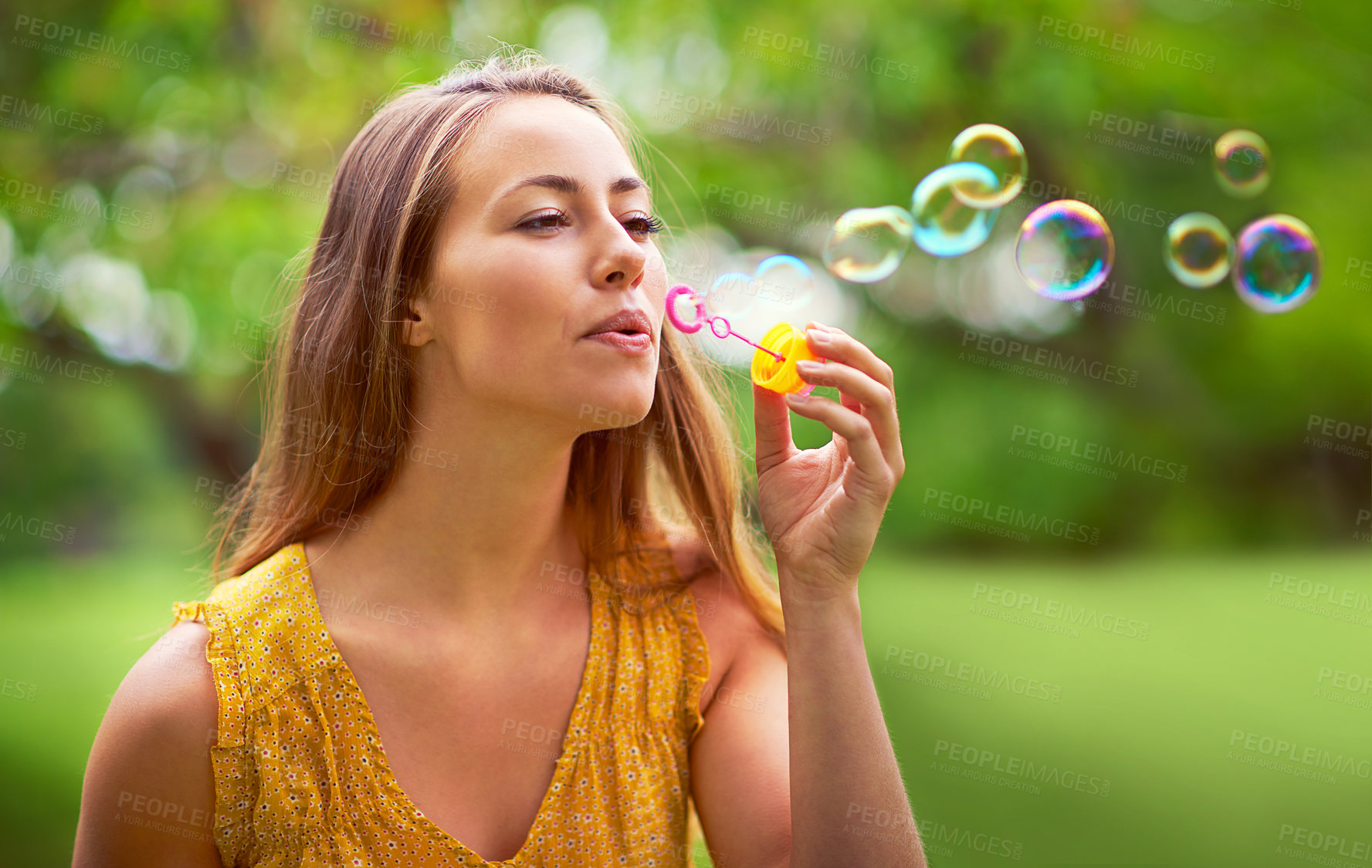 Buy stock photo Shot of a carefree young woman blowing bubbles in the park