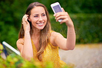 Buy stock photo Shot of a carefree young woman taking a selfie on her phone at the park