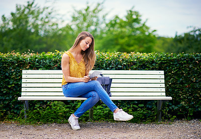 Buy stock photo Shot of a young woman using a digital tablet on a park bench
