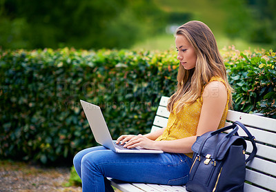 Buy stock photo Shot of a young woman using a laptop on a park bench