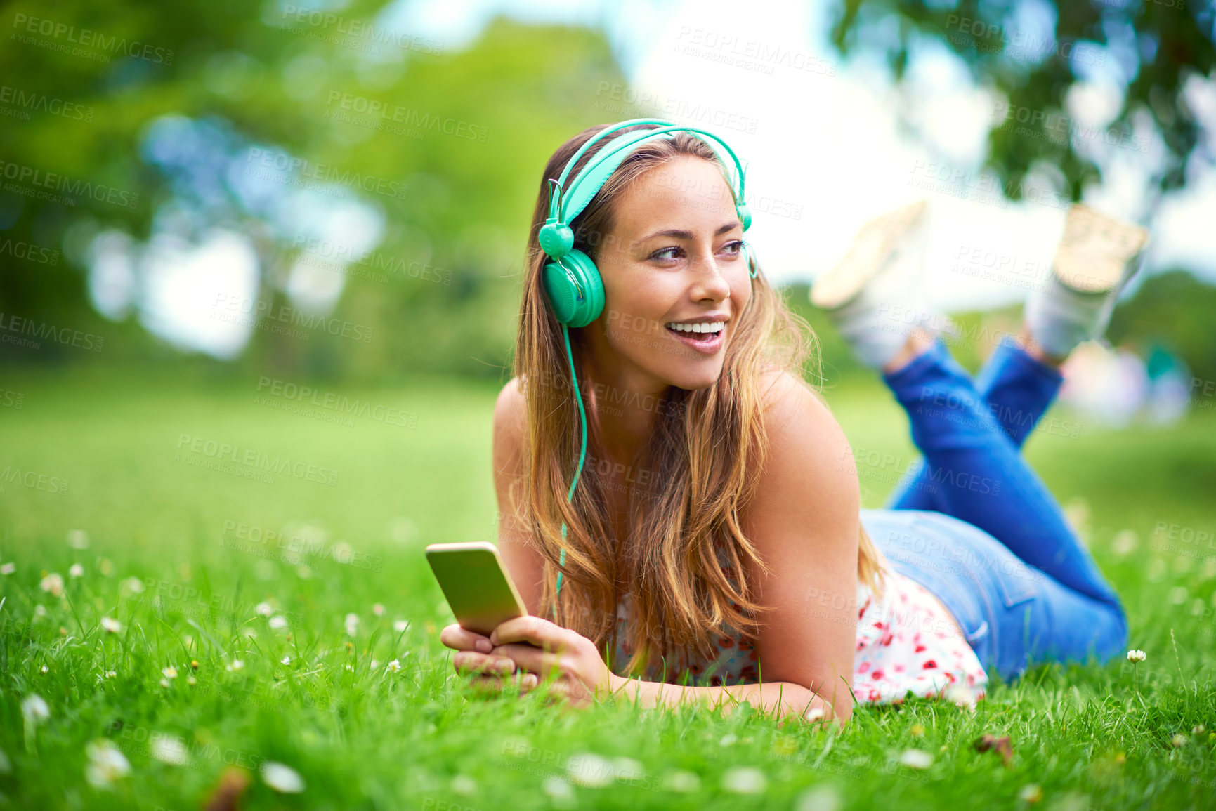 Buy stock photo Shot of a young woman listening to music while lying on the grass at the park