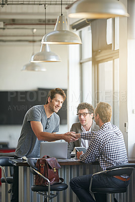 Buy stock photo Shot of two colleagues shaking hands while working together in a modern office