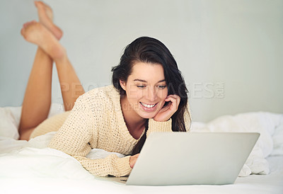 Buy stock photo Cropped shot of a young woman using her laptop while lying on her bed