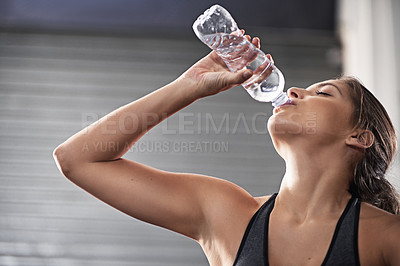 Buy stock photo Cropped shot of a young woman drinking from her water bottle at the gym