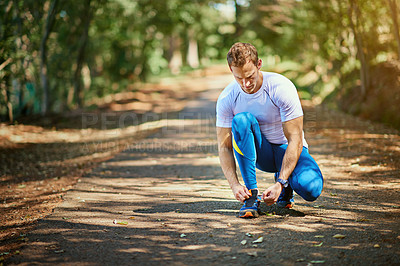 Buy stock photo Shot of a young man tying his shoelaces before a trail run