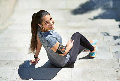 Buy stock photo Shot of a sporty young woman listening to music while sitting on steps outside