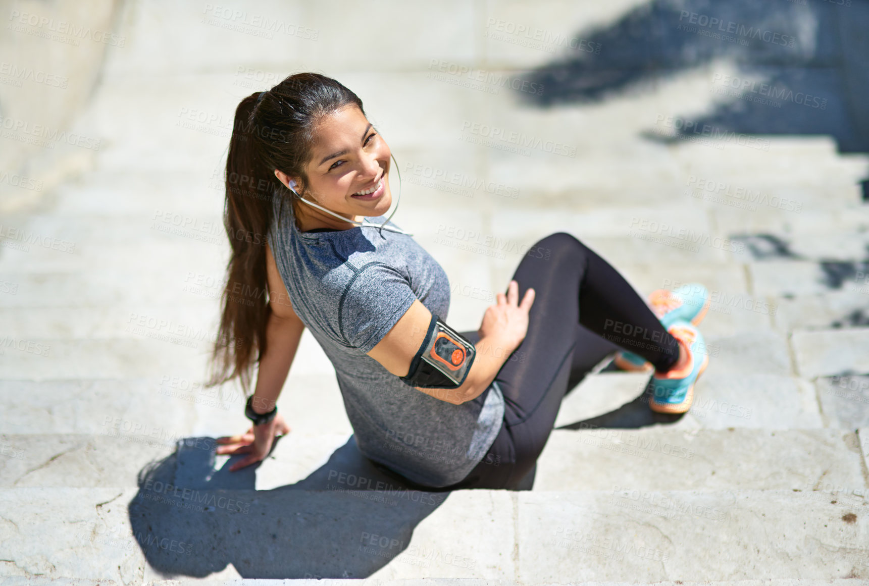 Buy stock photo Shot of a sporty young woman listening to music while sitting on steps outside