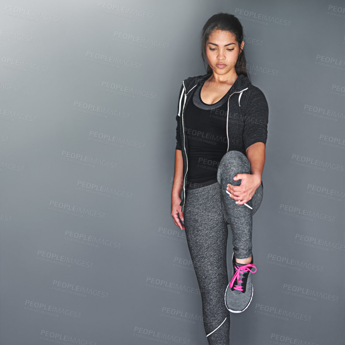 Buy stock photo Shot of a fit young woman stretching her legs against a gray background