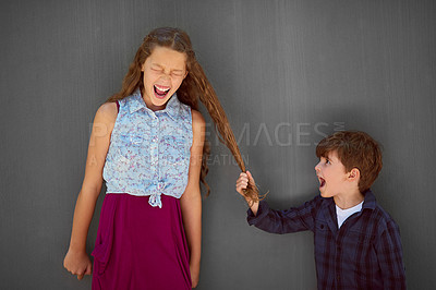 Buy stock photo Studio shot of a young boy pulling his sister's hair while standing against a gray background