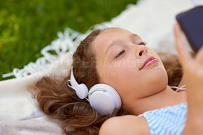 Buy stock photo High angle shot of a young girl listening to music on her cellphone while lying on a blanket outside